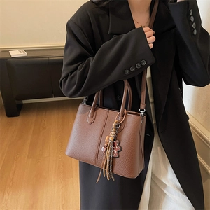Detail of dark brown lychee texture tote bag with teddy bear charm and tassel
