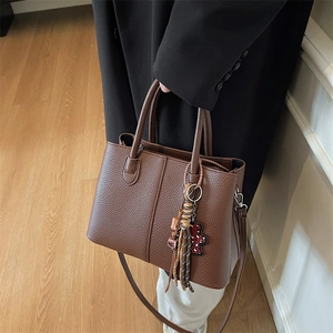 Detail view of large brown leather tote bag with tassels and leopard print bear pendant