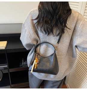 Détail du sac demi-lune noir en similicuir avec breloque perlée et bandoulière amovible