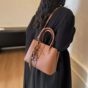Close-up of brown pebbled leather tote bag with woven tassel and leopard print bear charm