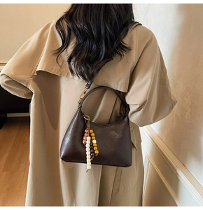Détail du sac hobo en cuir marron foncé avec breloque en perles de bois sur manteau beige