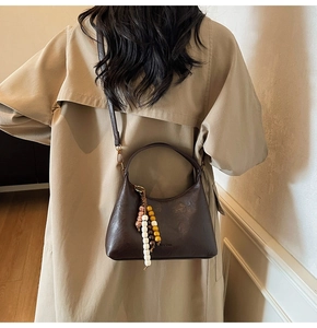 Sac bandoulière marron foncé avec charme perlé porté par un mannequin en trench