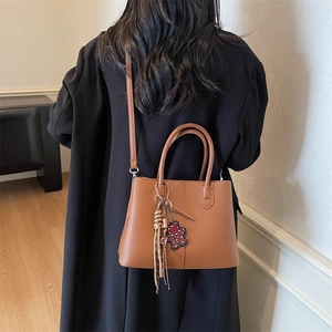 Brown lychee leather tote bag with silk scarf and red bear charm worn on the shoulder