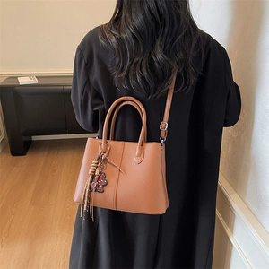 Brown litchi grain tote bag with bear charm shown on model in a modern interior