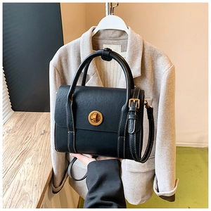 Detail of a vintage black crossbody bag featuring a golden twist lock and white contrast stitching
