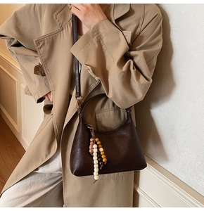 Détail du sac hobo en cuir marron foncé avec breloques de perles sur la bandoulière