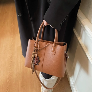 Detail of brown litchi leather tote bag with tassel charm and bear accessory pendant