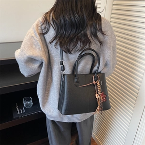 Close-up of black lychee grain tote bag featuring a cute bear tassel charm detail