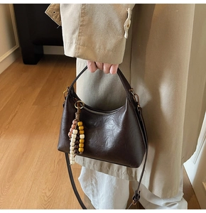 Détail d'un sac demi-lune marron foncé avec pendentif en perles et bandoulière amovible