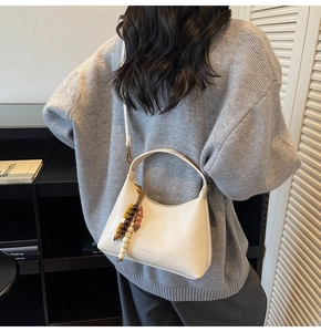 Sac hobo en cuir blanc avec pompon perlé et bandoulière porté par un mannequin