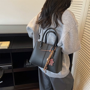 Detailed close-up of a large black tote bag with animal charm and tassel on a model