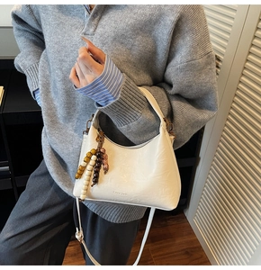Détail du sac bandoulière blanc en demi-lune avec breloque perlée et texture cuir