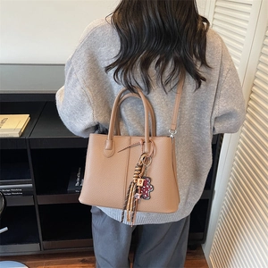 Brown litchi leather tote bag with tassel charm worn by model in a library setting
