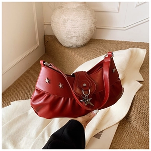 Close-up of red ruched crescent bag with silver star studs and metal pendant charm