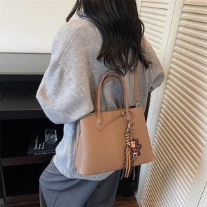 Detailed shoulder view of a brown pebbled leather tote bag with tassels and charm