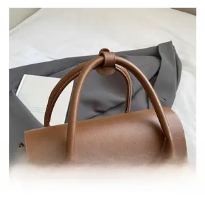 Close-up of brown vintage handbag with gold clasp and dual handles on white surface