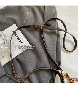 Détail de la bandoulière en cuir marron avec boucle réglable en métal doré sur gris