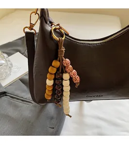 Détail du sac bandoulière en cuir marron foncé avec breloque en perles de bois et logo