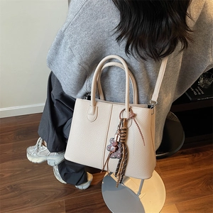 Detail of cream tote bag featuring lychee leather texture and cute bear pendant charm