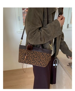 Detail of leopard print tote bag featuring leather handles and a plush tassel charm