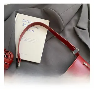 Detail of red crescent bag featuring silver star rivets and elegant pleats on a blazer