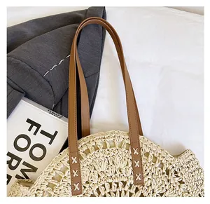 Close-up of woven straw tote bag with brown leather straps and cross-stitch detail