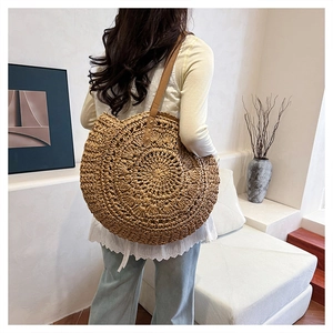 Detail of a large woven straw shoulder bag with leather straps on a female model's back