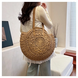 Detail of round straw tote bag with brown leather straps and intricate woven texture