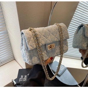 Close-up of light blue tweed quilted handbag with golden chain and metallic twist lock