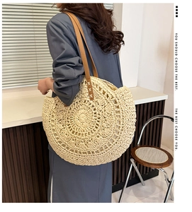 Model wearing a round straw knit tote bag with brown leather straps and hollow pattern