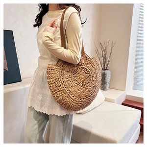 Detail of a woven straw tote bag with brown leather straps shown on a model