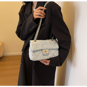 Detail of light blue tweed quilted shoulder bag with gold chain strap on a black blazer