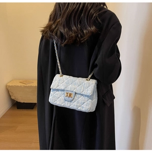 Close-up of light blue tweed quilted handbag with golden chain strap and twist lock detail