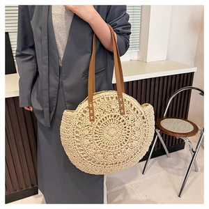 Detail of round straw tote bag with brown leather straps and cross-stitch detailing