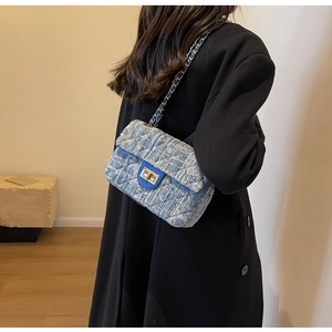 Blue and white tweed quilted chain bag worn over a black coat in a studio setting