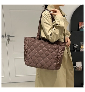Detailed view of dark brown quilted tote bag with wide shoulder strap on model