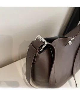Detail of adjustable long shoulder strap on a dark brown leather tote with silver buckle