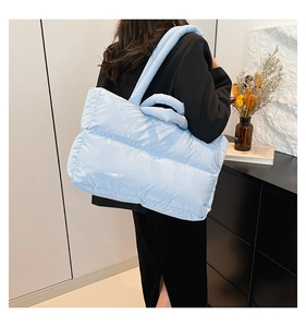 Sky blue padded tote bag with glossy finish shown on model in a stylish interior setting