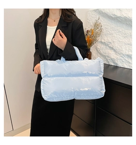 Close-up of light blue quilted puffer tote bag styled with a black blazer jacket