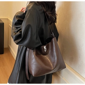Detail of dark brown leather tote bag with silver buckle worn with a black coat