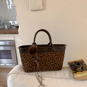 Leopard print crossbody bag with brown leather trim and plush charm on casual sofa