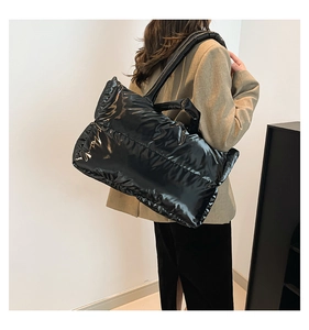 Detail of glossy black quilted puffer tote bag with wide shoulder strap worn by model