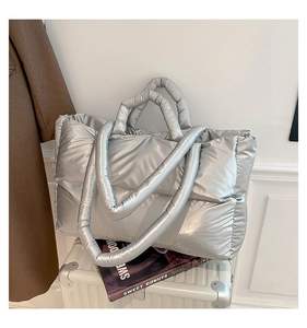 Detail of silver metallic puffer tote bag with quilted texture on a white suitcase