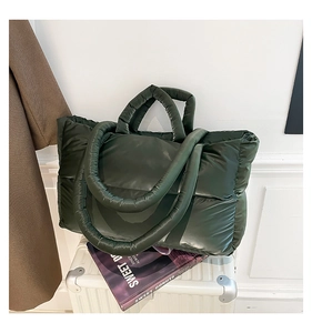Detail of dark green quilted puffer tote bag with glossy texture on white luggage
