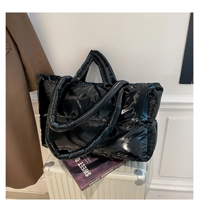 Close-up of black glossy padded tote bag placed on a white suitcase in a travel setting