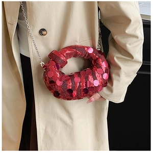 Detail of red sequined crescent bag with knot handle and silver chain on beige coat