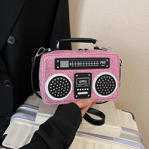 Pink sequin crossbody bag in vintage radio shape with leather handle on a suitcase