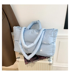 Detail of light blue quilted puffer tote bag with glossy texture on white suitcase