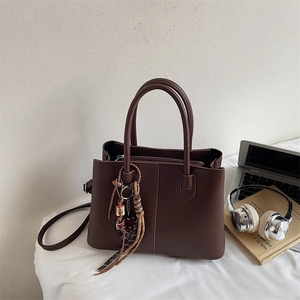 Brown lychee leather tote bag with double handles and tassel charm in a lifestyle office setting