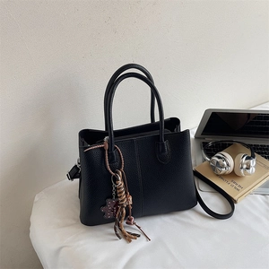 Black litchi grain leather tote bag with heart charm and crossbody strap in office setting